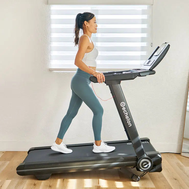 Female walking on a treadmill in the incline position in a living room with soft lighting.